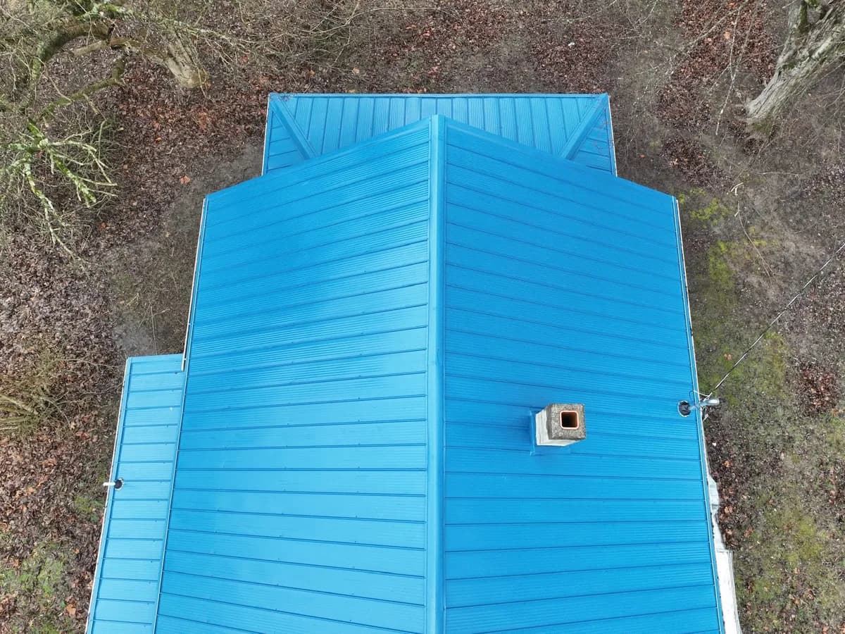 Bright blue metal roof viewed from above, with a chimney and intersecting roof sections